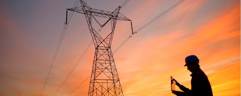 Electricien devant une tour électrique sur fond de coucher de soleil.