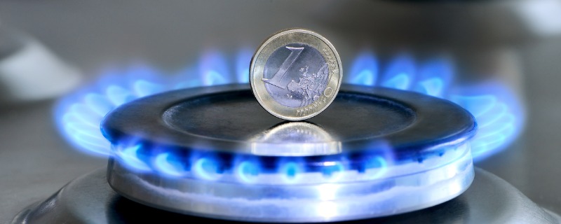 Pièce de un euro sur la tranche se trouvant sur une plaque de cuisson au gaz allumée.
