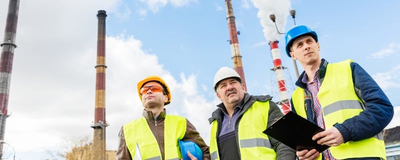 Trois ouvriers de construction devant quatre cheminées d'usine.