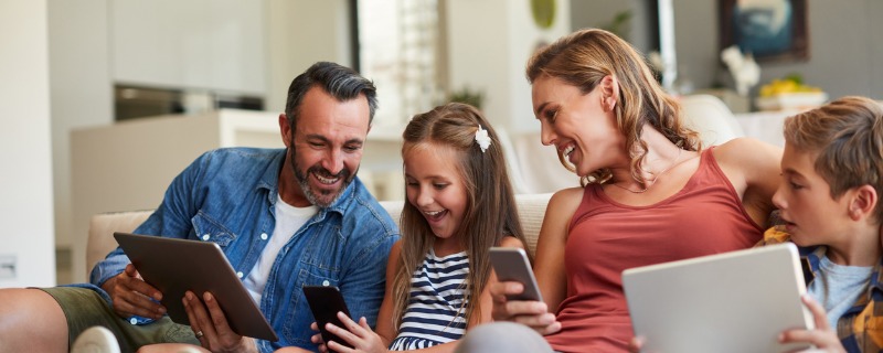 Famille souriante dont chaque membre est sur un appareil relié a internet différent.