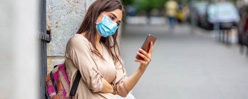 Jeune femme portant un masque chirurgical regarde son téléphone en rue.