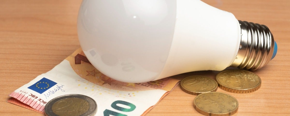 Concept de coût de l’énergie: ampoule sur une table en bois avec billet en euros et pièces de monnaie