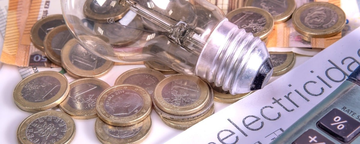 Concept de coût de l’énergie: ampoule sur une table avec billet en euros, pièces de monnaie, une facture d'électricité et une calculette