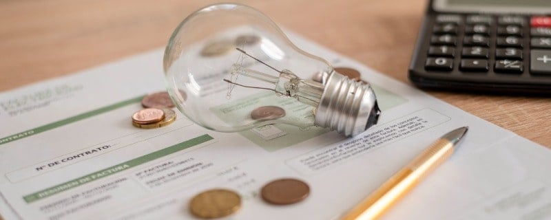 Facture d'électricité avec une ampoule, plusieurs pièces de monnaie, une calculatrice et un stylo sur le bureau. 