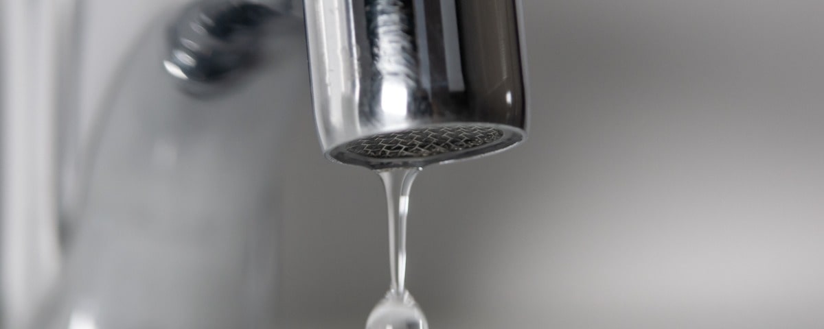 Macrophotographie d'un robinet chromé qui goutte de l'eau.