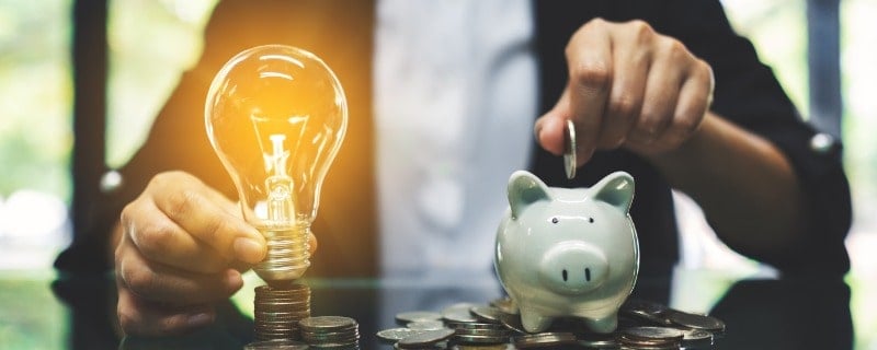 image conceptuelle d'économies d'énergie représentant une femme d’affaires mettant la pièce de monnaie dans la tirelire et une ampoule au-dessus de la pile de pièces de monnaie sur la table
